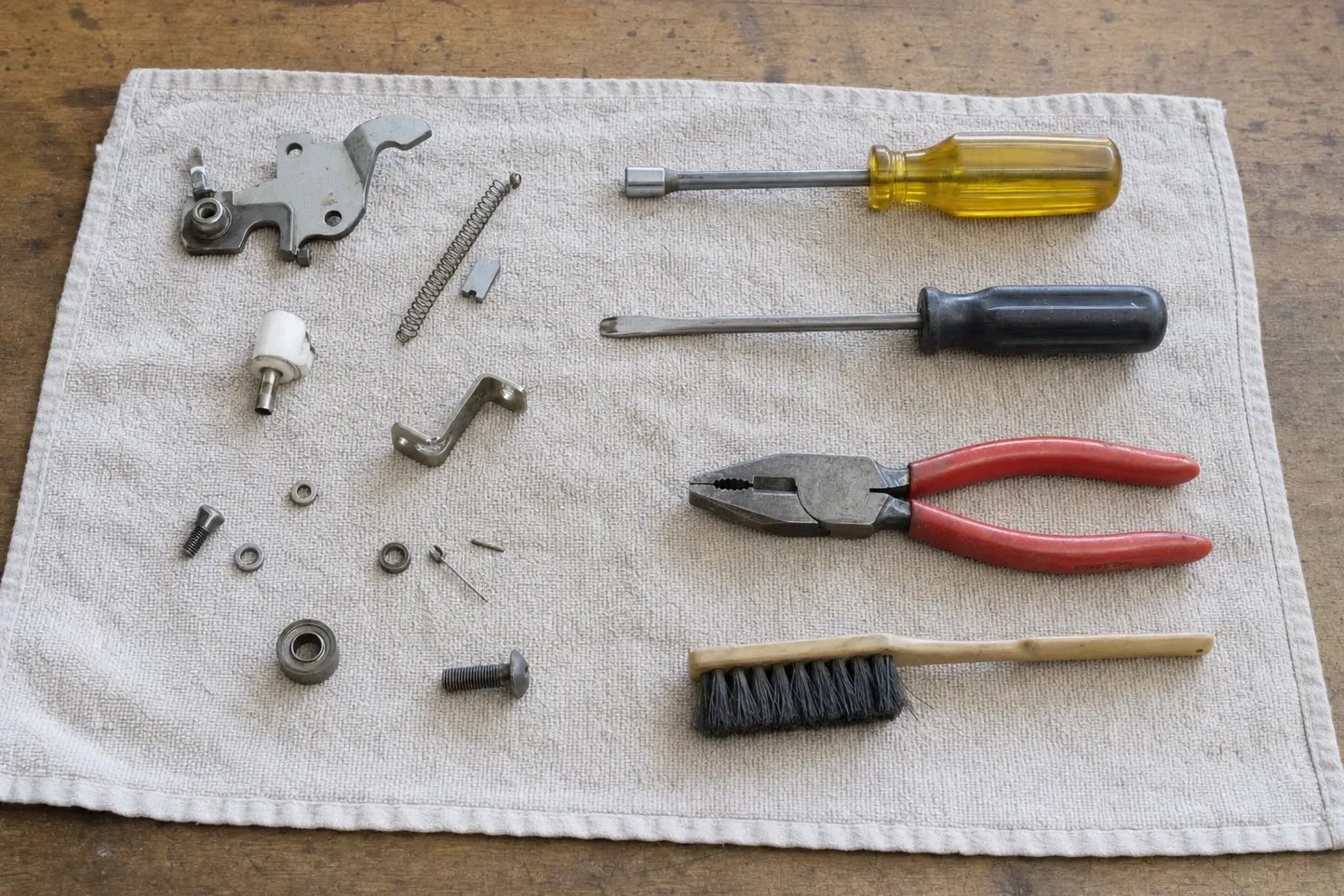 Stripped latch hardware — bracket, spring, ceramic insulator and a small bearing — on a cloth beside a nut driver and pliers
